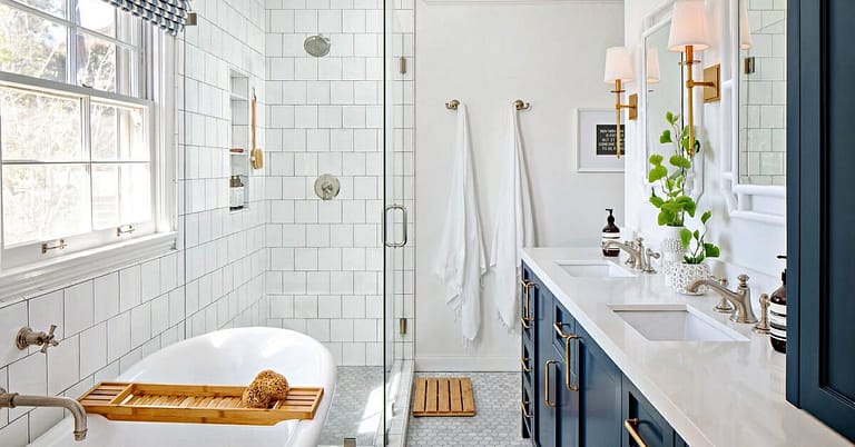 Modern bathroom renovation ideas showcased in a space with white subway tiles, a freestanding bathtub with a bamboo caddy, a clear glass walk-in shower, and a navy blue vanity with double sinks and gold fixtures, bathed in natural light.